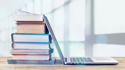 Stack of books with laptop on wooden table