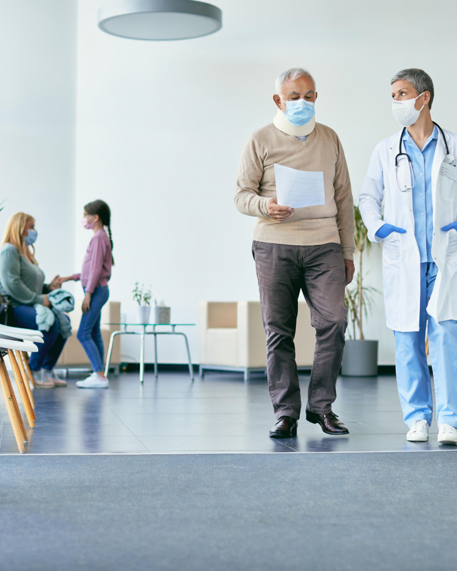 Senior patient with neck collar and his doctor analyzing medical report while walking through hallway at the hospital.